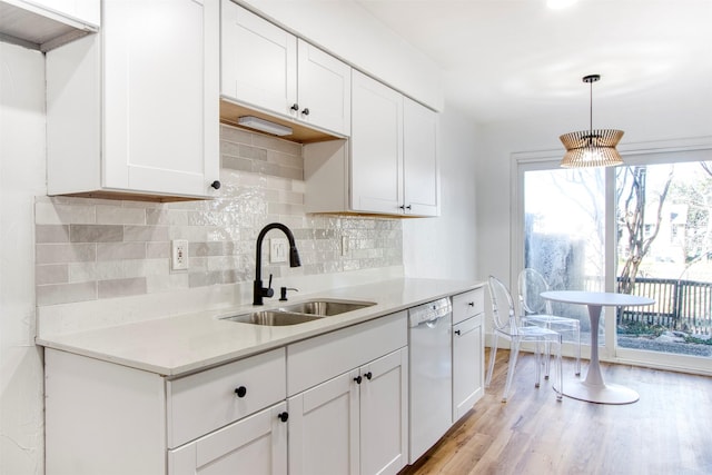 kitchen with tasteful backsplash, light countertops, light wood-style floors, a sink, and dishwasher