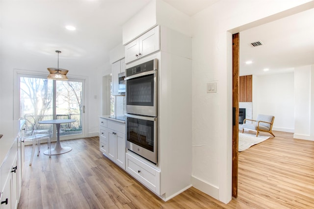 kitchen featuring light wood finished floors, stainless steel double oven, a glass covered fireplace, white cabinets, and baseboards