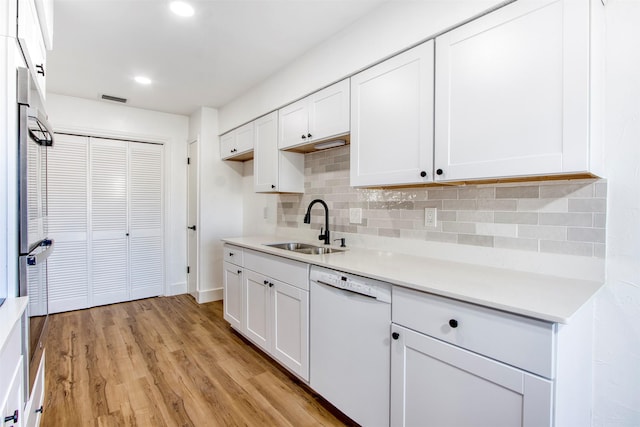 kitchen featuring light wood finished floors, visible vents, white cabinets, white dishwasher, and a sink