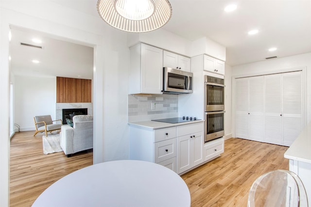 kitchen with tasteful backsplash, stainless steel appliances, light countertops, light wood-style floors, and white cabinetry