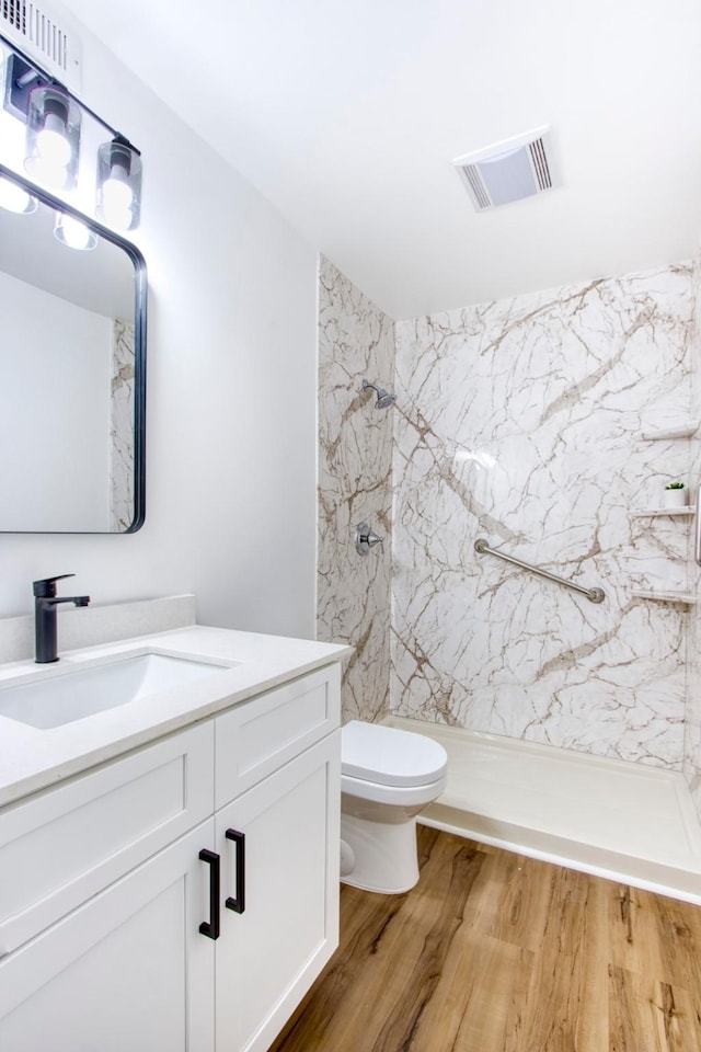 full bathroom with a marble finish shower, visible vents, toilet, wood finished floors, and vanity