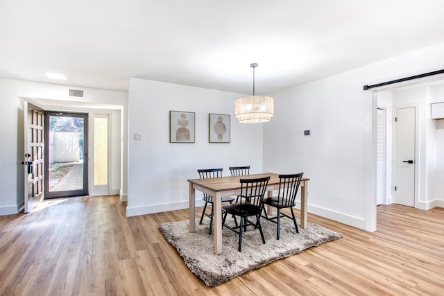 dining area with light wood finished floors, a barn door, visible vents, baseboards, and an inviting chandelier