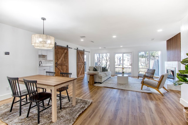 dining room with recessed lighting, a tiled fireplace, a barn door, light wood-type flooring, and baseboards