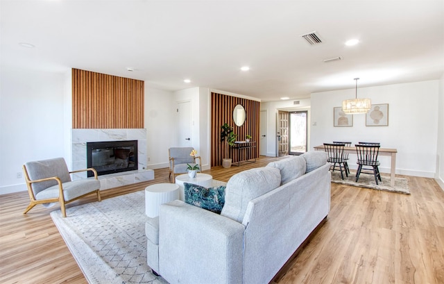 living room featuring light wood-style flooring, recessed lighting, a high end fireplace, visible vents, and baseboards