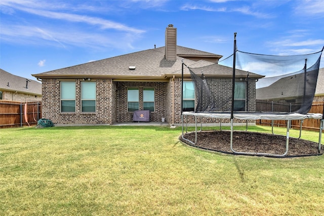 rear view of property with a trampoline, a fenced backyard, and a lawn