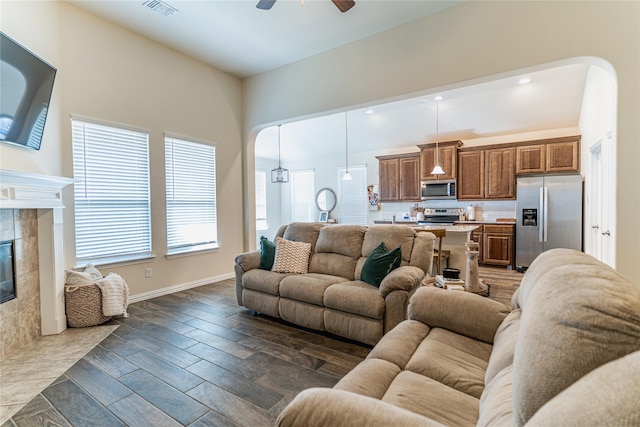 living area featuring dark wood-style flooring, visible vents, a ceiling fan, a tile fireplace, and baseboards