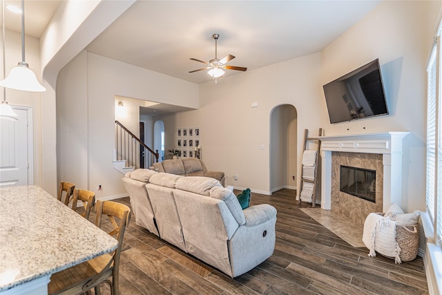 living area featuring arched walkways, a ceiling fan, a tiled fireplace, stairway, and wood tiled floor