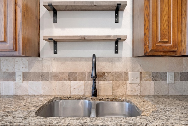 kitchen with light stone countertops, brown cabinetry, backsplash, and a sink