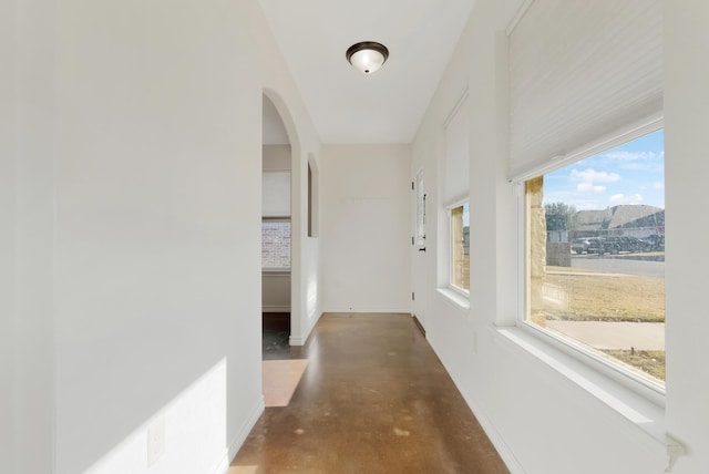 hall featuring finished concrete flooring, baseboards, and arched walkways