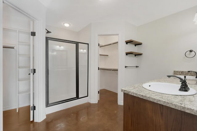 full bathroom with vanity, baseboards, a shower stall, a walk in closet, and finished concrete floors