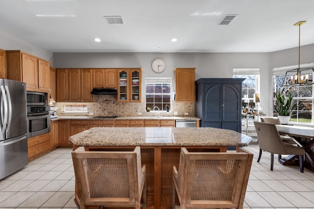 kitchen with appliances with stainless steel finishes, a kitchen island, visible vents, and under cabinet range hood