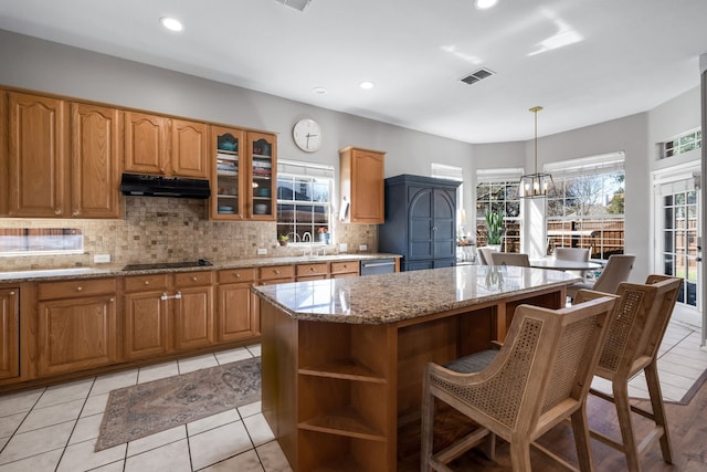 kitchen featuring light stone counters, under cabinet range hood, a kitchen island, visible vents, and stainless steel dishwasher