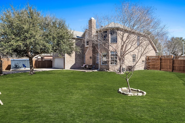 exterior space with driveway, a garage, a lawn, a fenced backyard, and a chimney