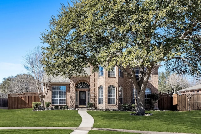 view of front of house with brick siding, a front yard, and fence