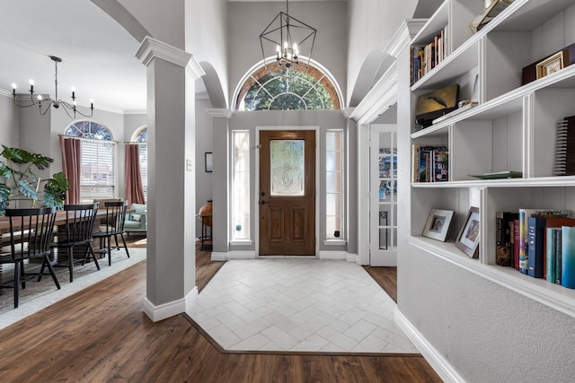 foyer entrance featuring baseboards, wood finished floors, a high ceiling, ornate columns, and a notable chandelier