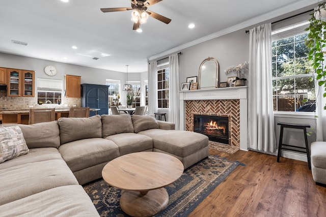 living room with dark wood-style flooring, visible vents, a tiled fireplace, and a healthy amount of sunlight