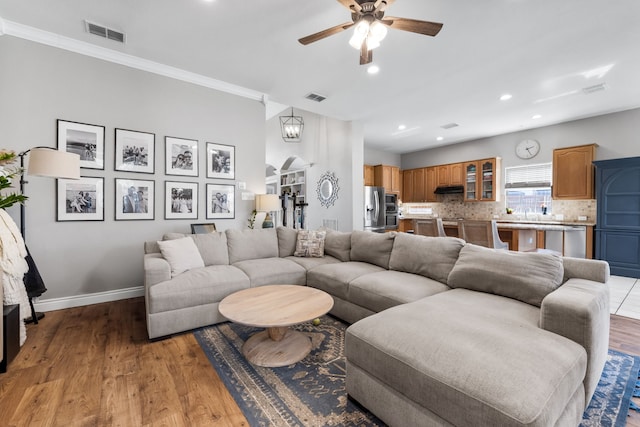 living room with crown molding, light wood-type flooring, visible vents, and baseboards