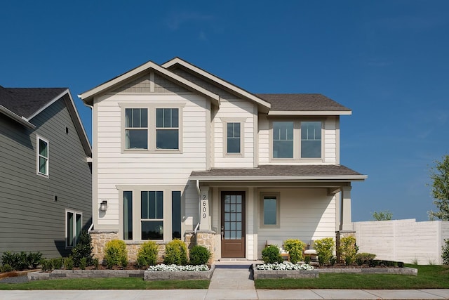 craftsman-style home with a shingled roof, stone siding, and fence