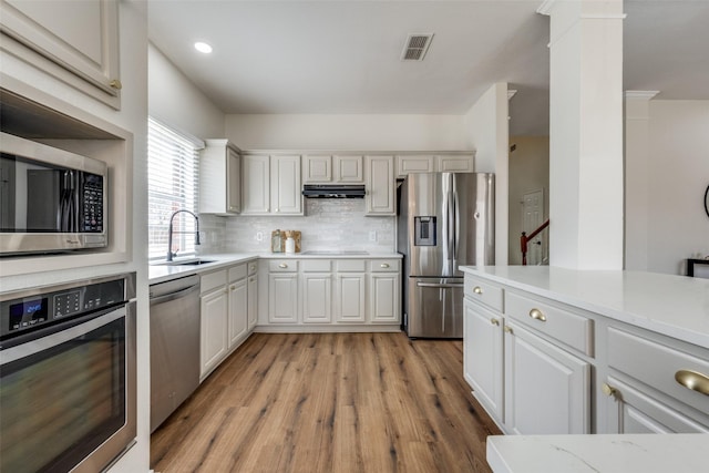 kitchen featuring under cabinet range hood, a sink, visible vents, appliances with stainless steel finishes, and tasteful backsplash