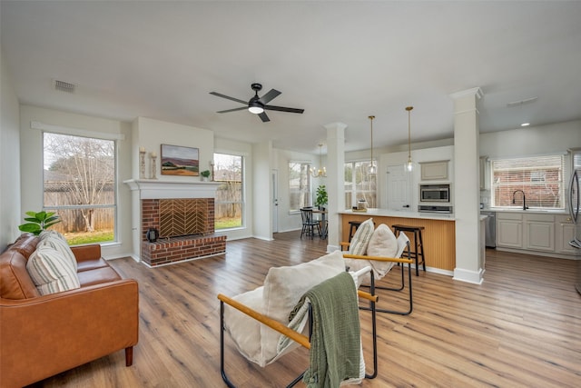 living area featuring light wood finished floors, a brick fireplace, decorative columns, and visible vents