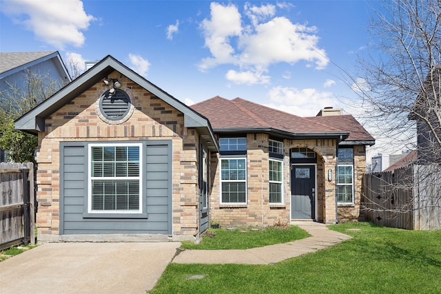 view of front of house featuring brick siding, a front lawn, fence, roof with shingles, and a chimney