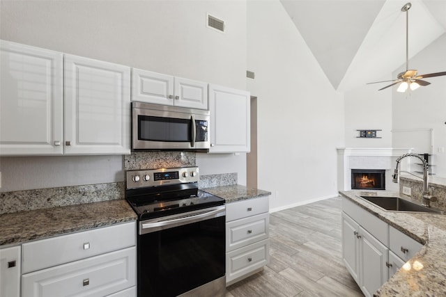 kitchen featuring visible vents, a sink, appliances with stainless steel finishes, a brick fireplace, and light wood-type flooring