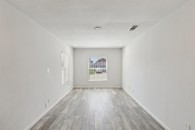 empty room with visible vents, baseboards, light wood-style floors, and a textured ceiling