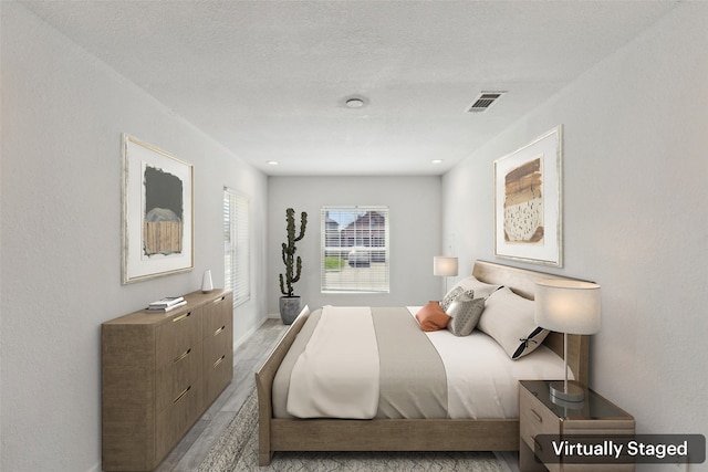 bedroom featuring light wood-style floors, visible vents, and a textured ceiling