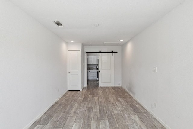 empty room with visible vents, recessed lighting, a barn door, light wood finished floors, and baseboards