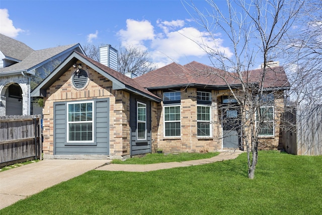 view of front of home with fence, a front yard, a shingled roof, brick siding, and a chimney