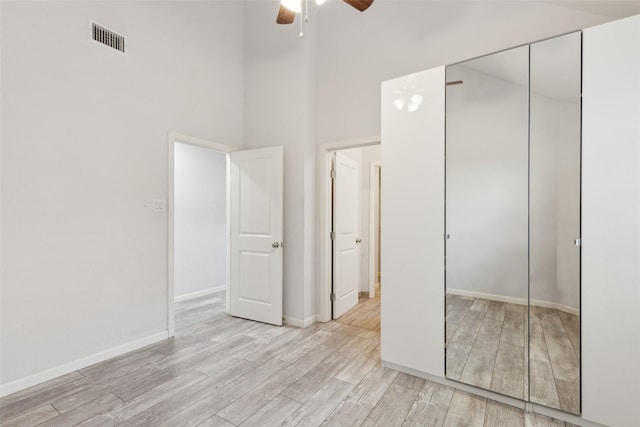 unfurnished bedroom with visible vents, baseboards, light wood-style flooring, a towering ceiling, and a closet