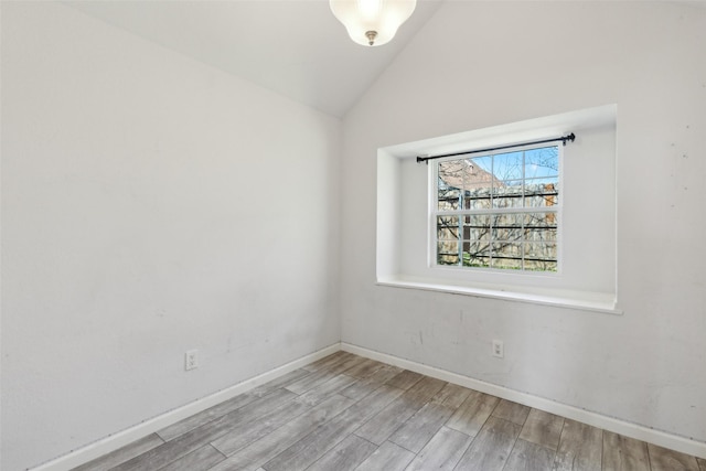 empty room featuring wood finished floors, baseboards, and vaulted ceiling