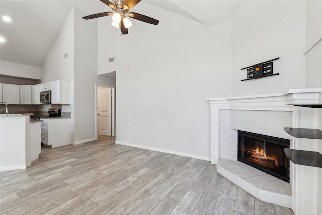 unfurnished living room with visible vents, baseboards, light wood-style flooring, a fireplace, and a ceiling fan