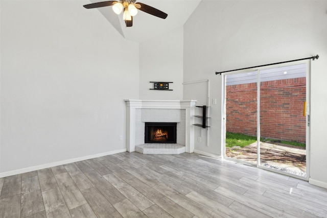 unfurnished living room featuring ceiling fan, baseboards, a fireplace, wood finished floors, and high vaulted ceiling