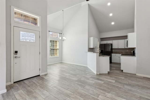 entryway with a notable chandelier, light wood-style floors, baseboards, and high vaulted ceiling