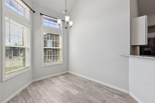 unfurnished dining area with wood finished floors, a notable chandelier, a healthy amount of sunlight, and baseboards