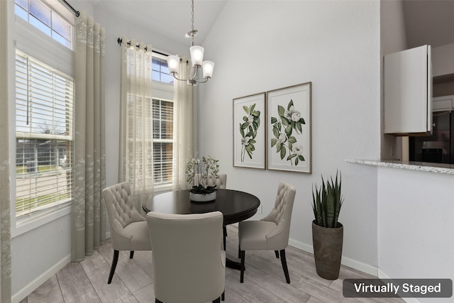 dining area featuring a chandelier, light wood-style flooring, baseboards, and lofted ceiling