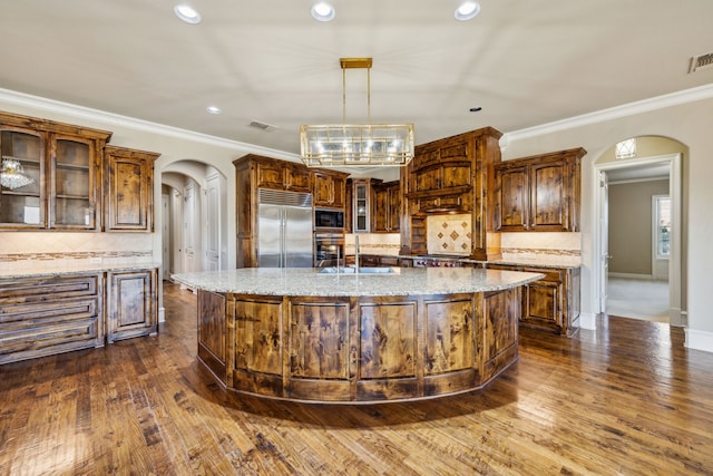 2161 Meadow View Dr, Prosper, TX 75078 - kitchen with arched walkways, built in appliances, tasteful backsplash, a kitchen island with sink, and glass insert cabinets