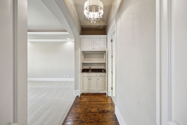 corridor featuring a sink, baseboards, a notable chandelier, and dark carpet