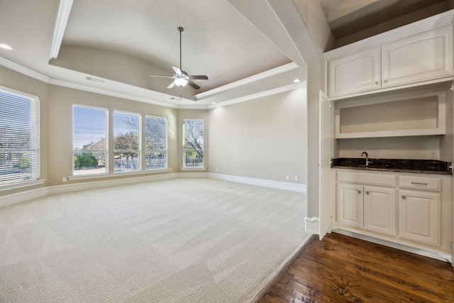 unfurnished living room featuring a raised ceiling, crown molding, baseboards, and dark carpet