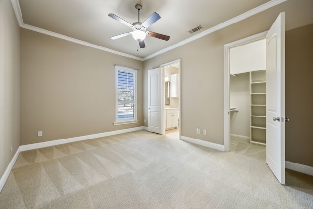 unfurnished bedroom featuring visible vents, light carpet, a walk in closet, crown molding, and baseboards