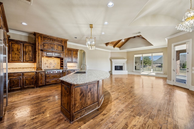 kitchen featuring a fireplace with raised hearth, a center island with sink, ornamental molding, a sink, and stainless steel gas cooktop