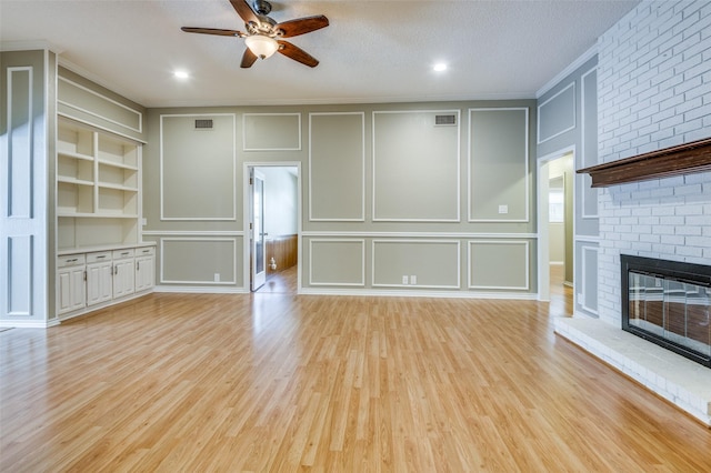 unfurnished living room with light wood finished floors, visible vents, a brick fireplace, built in shelves, and a decorative wall