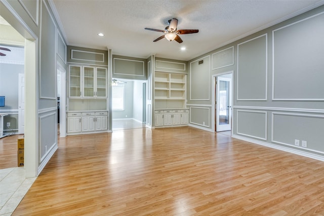 unfurnished living room featuring light wood-type flooring, ceiling fan, a decorative wall, and a textured ceiling