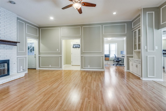 unfurnished living room with ornamental molding, light wood-type flooring, a brick fireplace, and a decorative wall