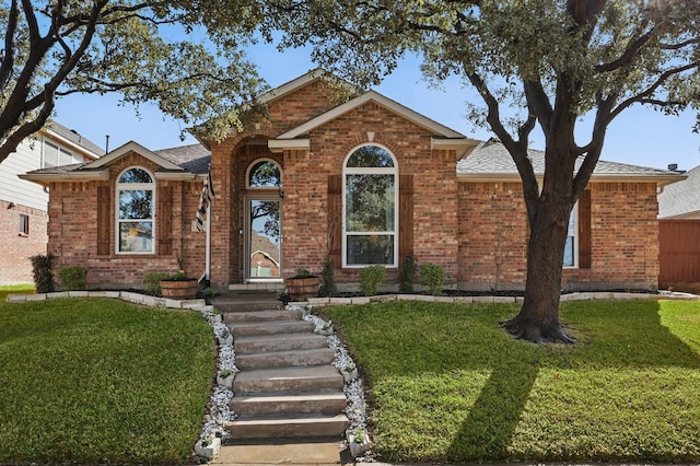 ranch-style home featuring brick siding, a front yard, and a shingled roof