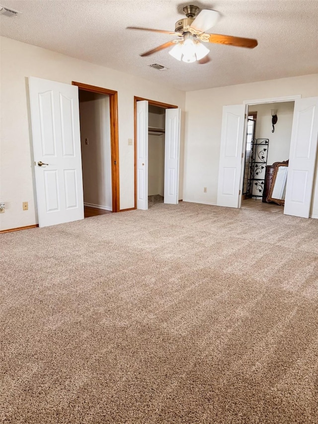 unfurnished bedroom with a textured ceiling, carpet floors, visible vents, baseboards, and a ceiling fan