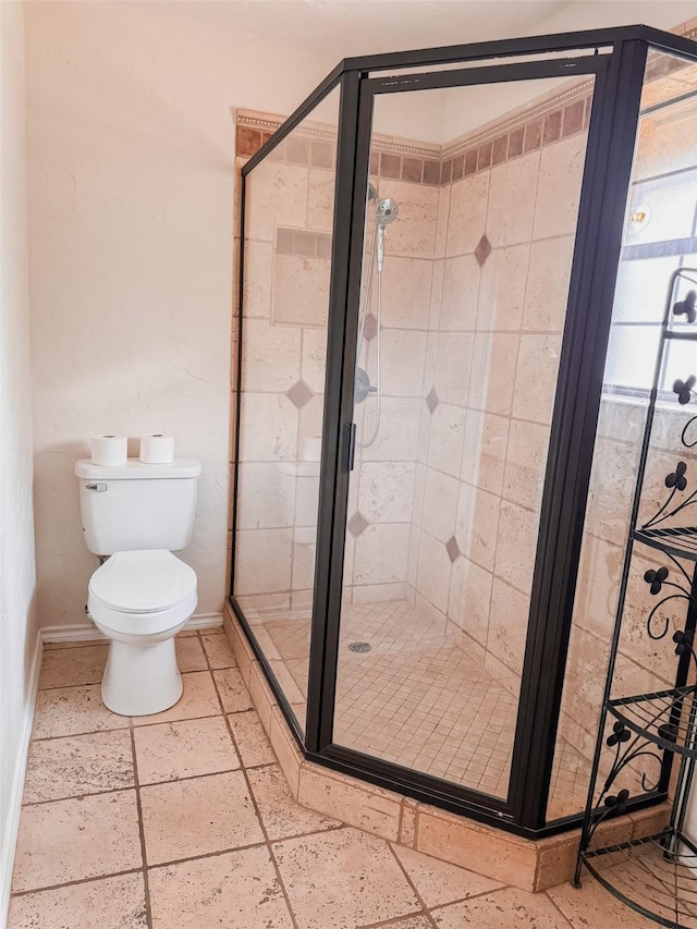 full bath with toilet, stone tile floors, baseboards, and a shower stall