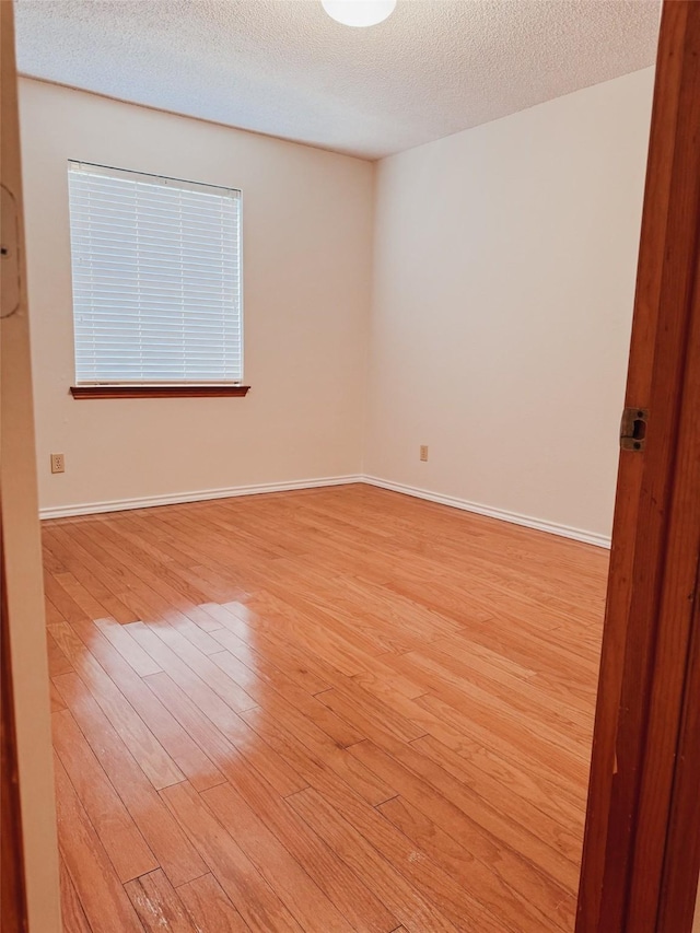 empty room with light wood finished floors, baseboards, and a textured ceiling