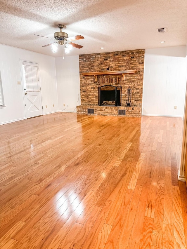 unfurnished living room featuring visible vents, a ceiling fan, light wood-style flooring, a textured ceiling, and a brick fireplace